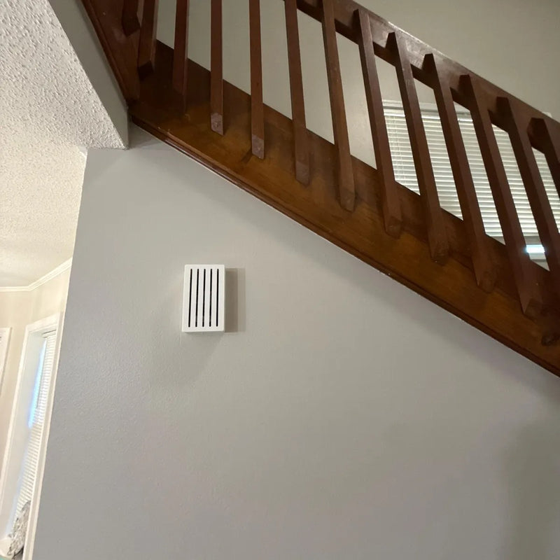 White Louver chime cover on a wall below a wooden staircase railing